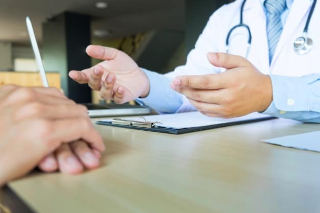 disclaimer: doctor names in this article have been anonymized for reasons regarding confidentiality, patient listening intently male doctor explaining patient symptoms asking question as they discuss paperwork together consultation